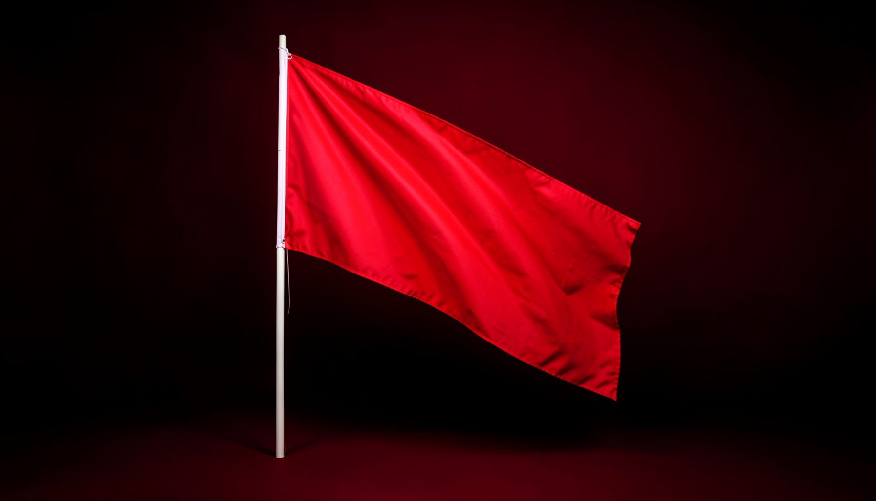 A dramatic studio photograph of a single red flag on a black seamless backdrop suggesting protest and tension